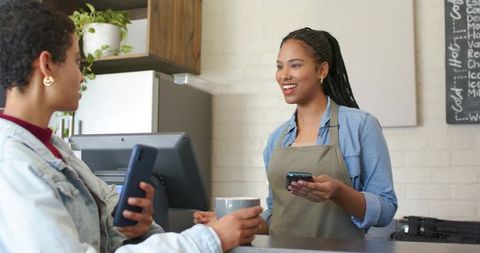 African american barista smiling while accepting mobile payment at cozy cafe counter
