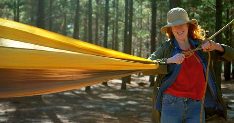 Woman setting up hammock in sunlit forest