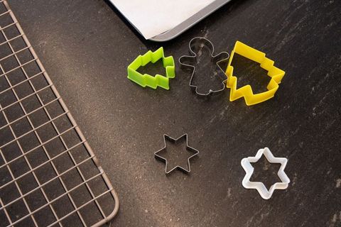 Holiday cookie cutters arranged on dark counter with cooling rack and parchment-lined tray