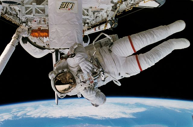 Historical image of an astronaut testing the Simplified Aid for EVA Rescue (SAFER) system outside the space shuttle Discovery. The Earth is visible in the background from 130 nautical miles above. Ideal for illustrating topics on space exploration, astronaut training, NASA missions, and space technology.
