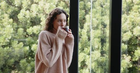 Woman enjoying hot drink by large window with nature background