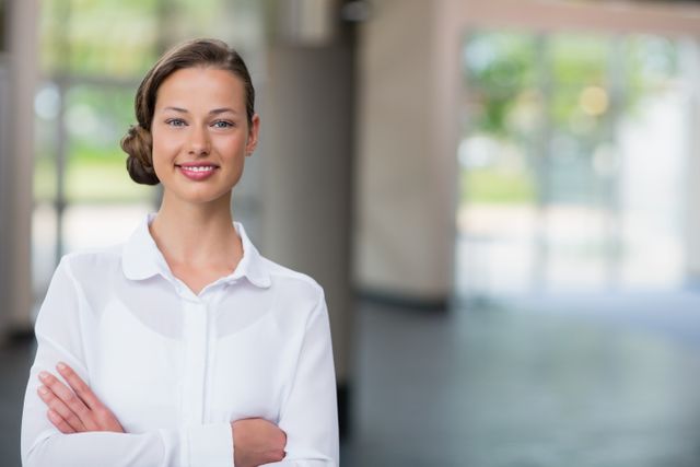 This image depicts a confident businesswoman standing with arms crossed in a modern office environment. Ideal for use in corporate websites, business presentations, leadership articles, and career development materials. It conveys professionalism, confidence, and success in a corporate setting.