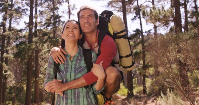 Middle-aged couple with backpacks hiking through a forest, showing joy and excitement of outdoor adventure. Ideal for travel blogs, outdoor activity promotions, or articles on relationships and lifestyles.