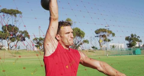 Athlete pressing kettlebell overhead on sports field outdoor strength training fitness