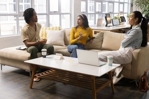 Diverse coworkers discussing project in bright modern office lounge with laptop and coffee