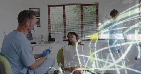 Smiling patient receiving dental care while dentist consulting and assistant adjusting lamp