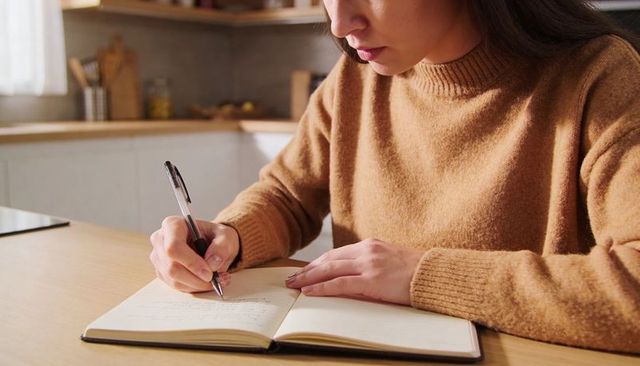 Cozy morning journaling woman writing in notebook at kitchen table with sunlit interior