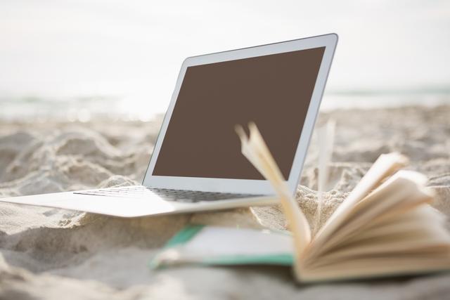 Open book and laptop on sand at beach