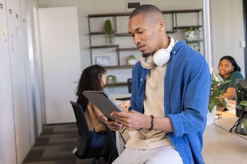 Focused young professional using tablet in collaborative casual coworking office with headphones