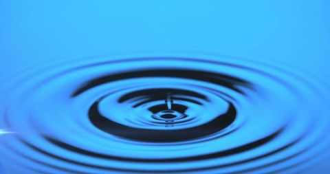 Water droplet causing concentric ripples on blue surface