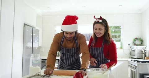 Couple baking christmas cookies in bright modern kitchen with santa hat and reindeer headband