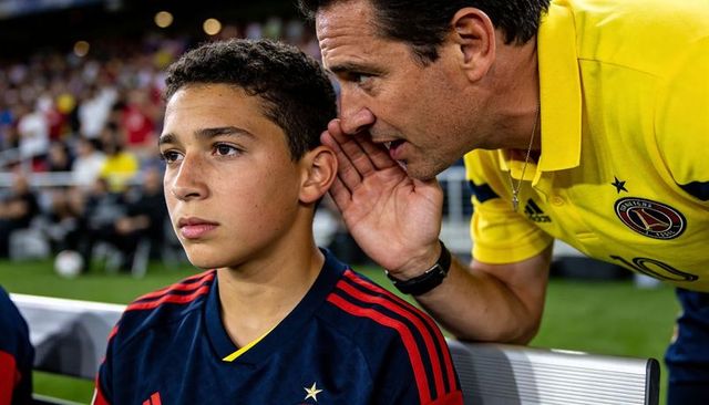 Youth soccer coach whispering tactics to focused bench player during match