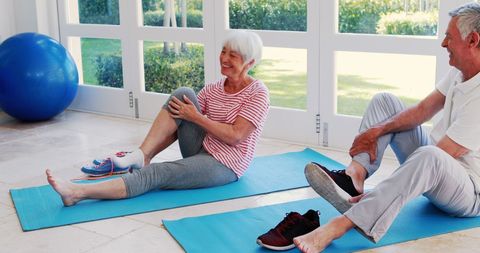 Senior Couple Stretching Together on Yoga Mats Indoors