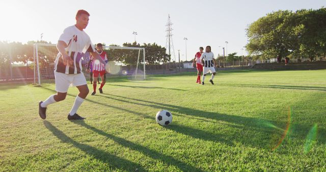Amateur soccer players competing on a sunny afternoon. Short shadows cast by the afternoon sun imply mid- to late-afternoon time. Ideal for use in advertisements for sportswear, soccer-related articles, blog posts on teamwork, or community event promotions.