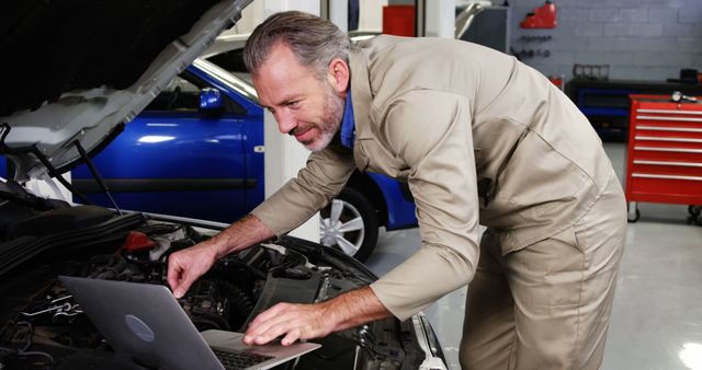 Experienced mechanic using laptop for vehicle diagnostics in car repair shop, combining traditional mechanical skills with modern technology. Ideal for illustrating car repair services, automotive technology integration, and professional mechanic services in promotional materials, articles on vehicle maintenance, or automotive workshops websites.