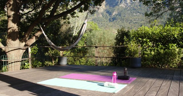 Two yoga mats, water bottles and towels on deck in sunny garden, copy space, slow motion. Yoga, wellbeing, tranquility, fitness, togetherness, nature and healthy lifestyle.