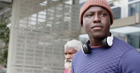 Young African American man wearing beanie and headphones on urban sidewalk