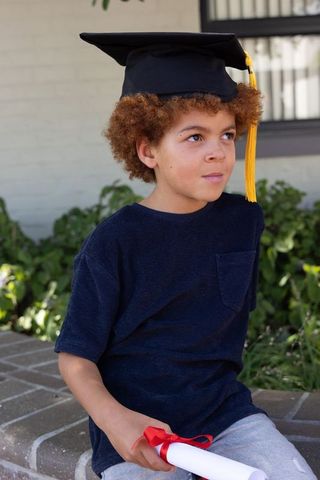 Young african american boy wearing graduation cap holding diploma in front yard portrait