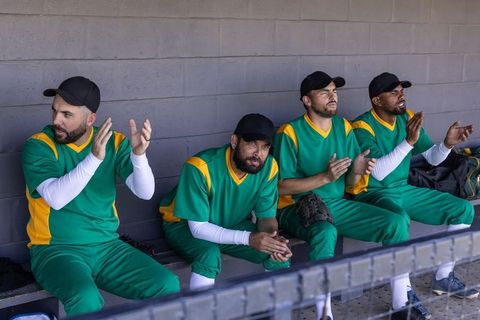 Green team baseball players sitting on dugout bench, clapping and cheering, showing unity