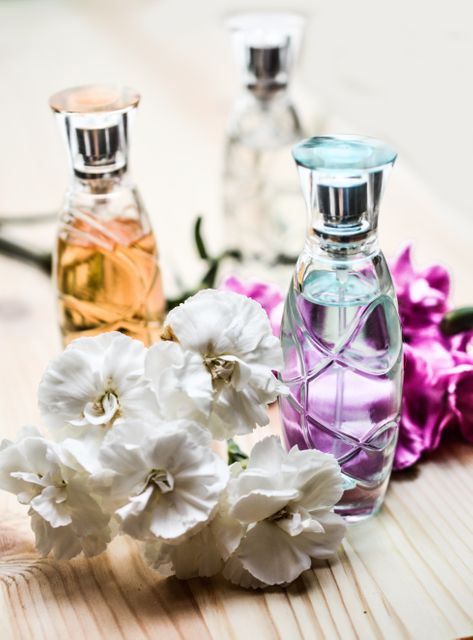 Various elegant perfume bottles displayed with fresh white and magenta flowers placed on a wooden surface create a luxurious and aromatic scene. This composition is ideal for use in beauty and fashion marketing materials, fragrance commercials, lifestyle blogs, and social media promotions.