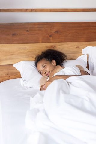 Woman hugging pillow lying in white bed with wooden headboard for cozy minimalist bedroom