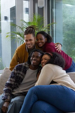 Diverse friends hugging and smiling on sofa in sunlit modern living room