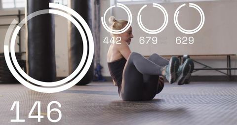 Mid-adult woman performing v-sit core exercise in gym wearing dark tank with digital hud
