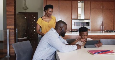 African american family gathering at kitchen island helping son use tablet for learning