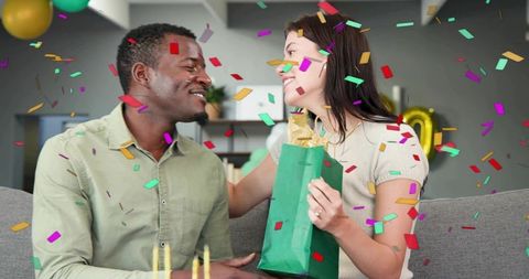 Couple exchanging gift celebrating birthday with confetti, balloons and lit candles