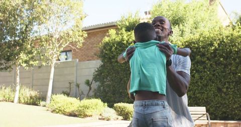 Father lifting young son in sunny backyard embracing playful outdoor family moment