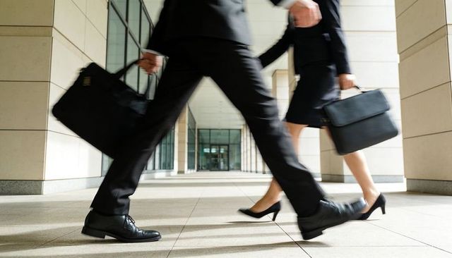 Two professionals striding through corporate corridor carrying black briefcases