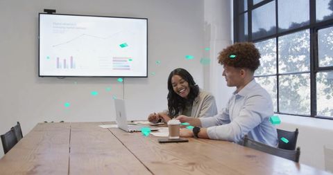 Two colleagues collaborating over laptop in bright modern meeting room with coffee