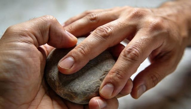 Hands cupping smooth river stone close-up fingertip tracing texture and grain mindfulness