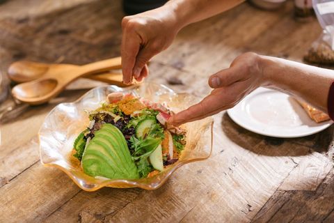 Hands garnishing vibrant avocado and citrus mixed greens salad on rustic wood table