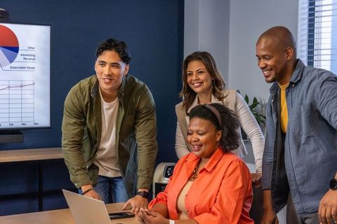 Diverse team collaborating around laptop reviewing analytics and growth charts in office