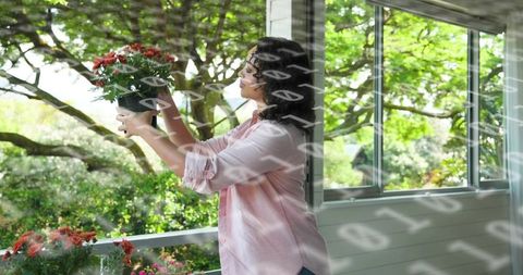 Woman placing potted flowers on sunroom ledge with sunlit porch and garden view