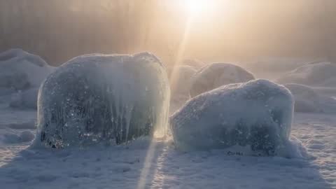 Sunrise Beam Casting Between Frosted Ice Boulders on Snowy Shoreline