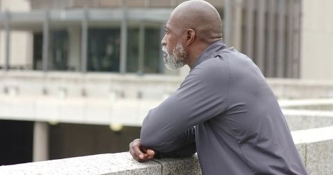 African American Man Leaning on Concrete Rail Gazing Over Urban Office Courtyard