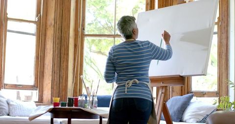 Senior woman painting canvas in sunny home art studio