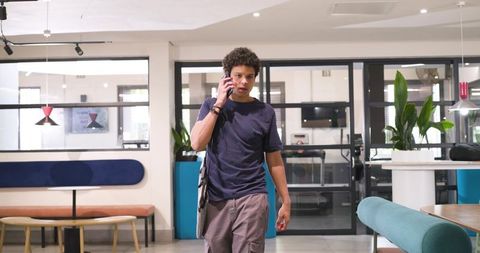 African american man talking on phone while walking through modern coworking lobby