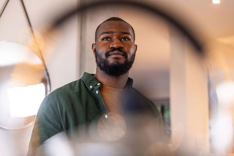 Confident african american man standing in warm home framed by circular mirrors