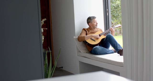 Man Playing Guitar Sitting on Window Seat at Home - Download Free Stock Images Pikwizard.com