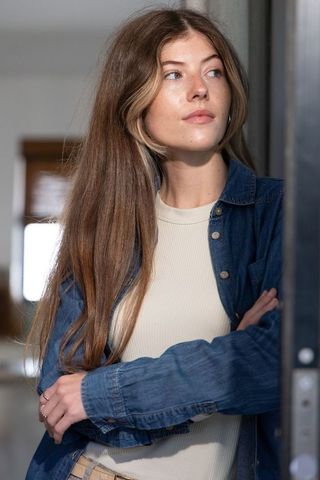Young woman standing in doorway leaning and looking contemplative wearing denim shirt and rings