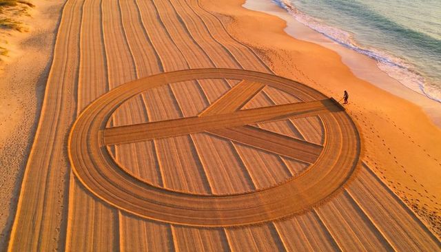 Beach artist raking giant geometric circle at sunrise creating concentric sand patterns