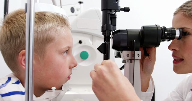 Optometrist examining young boy's eyes using specialized equipment, ideal for healthcare and medical articles, pediatric eye care promotions, vision health campaigns, or educational materials about eye exams for children.