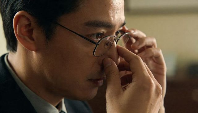 Asian man adjusting thin metal-rimmed glasses in office wearing suit and tie