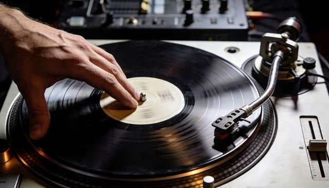 Dj hand cueing vinyl record on turntable with mixer and tonearm close-up for club music