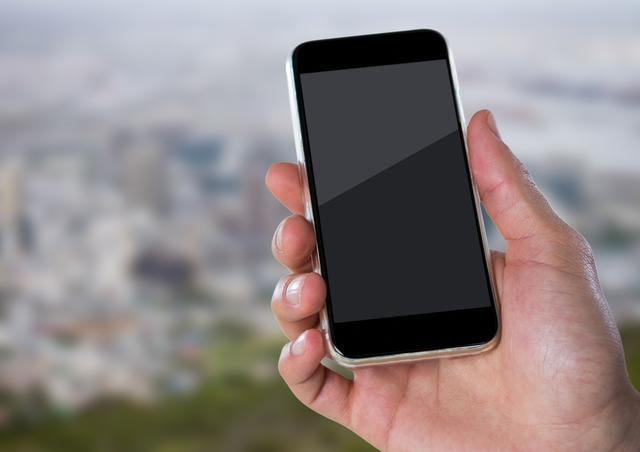 Person holding a smartphone with a blank screen in front of a blurred city skyline background. Useful for promoting mobile apps, technology services, or urban lifestyle concepts. Ideal as a visual for advertising, presentations, or website design where customizable screen space is needed.