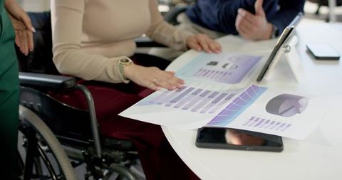Reviewing inclusive business analytics around meeting table with wheelchair and tablet