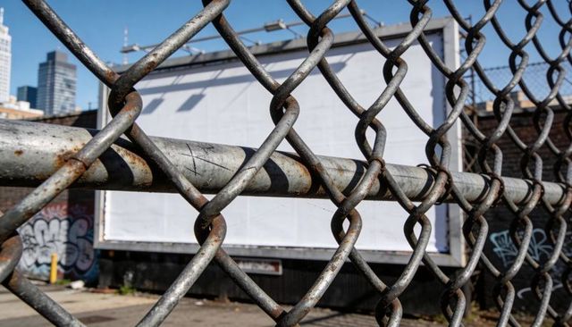 Rusted chain-link fence framing blank billboard, graffiti-covered urban vacant lot